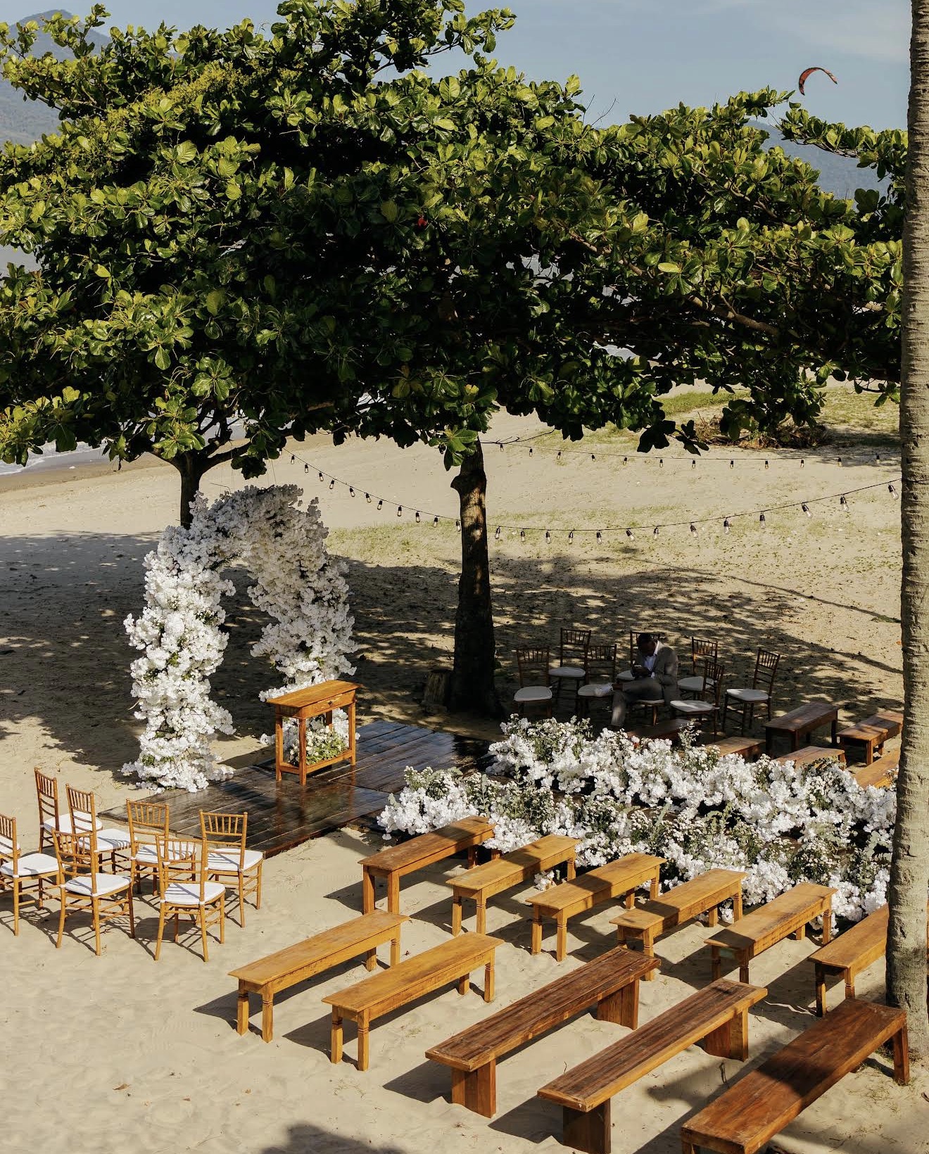 Cerimônia na areia com arco de flores brancas sob as árvores